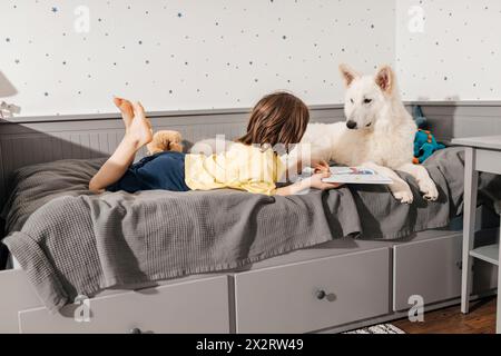 Boy lying on bed with white Swiss shepherd dog at home Stock Photo