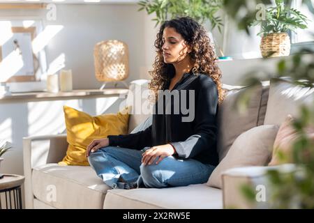 Young woman meditating on sofa at home Stock Photo