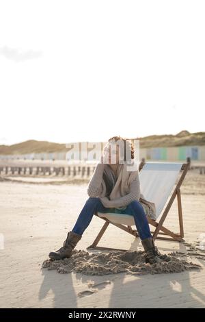 Thoughtful woman sitting on deck chair at beach Stock Photo