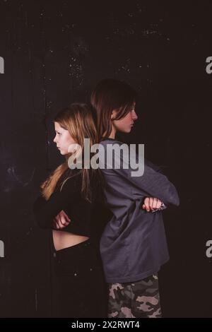 Angry friends standing back to back in front of black background Stock Photo