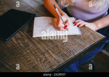 Young woman writing notes in diary at table in cafe Stock Photo