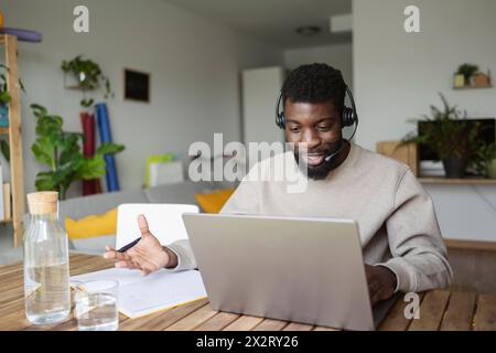 Smiling freelancer wearing headset and discussing on video call over laptop at home Stock Photo