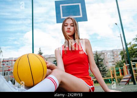 Basketball player sitting with ball in schoolyard Stock Photo