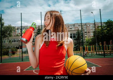 Basketball player holding water bottle in school yard Stock Photo