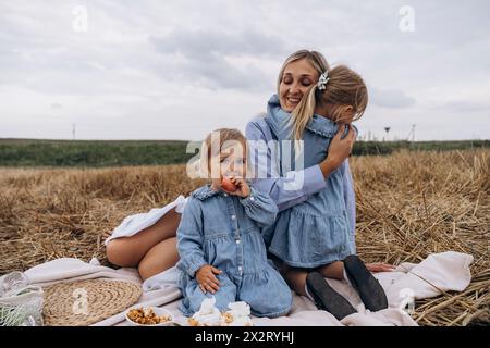 Happy woman enjoying picnic with daughters sitting on blanket over hay Stock Photo