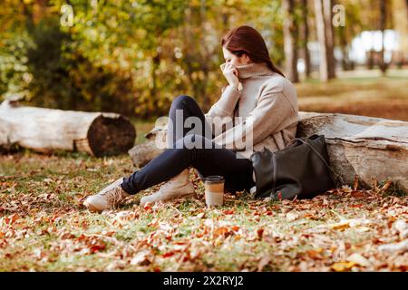 Mature woman covering face with turtleneck t-shirt and sitting near logs in park Stock Photo
