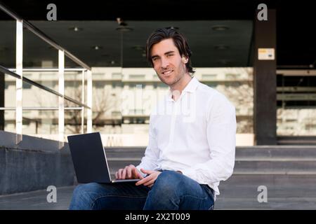 Smiling young businessman using laptop on steps Stock Photo