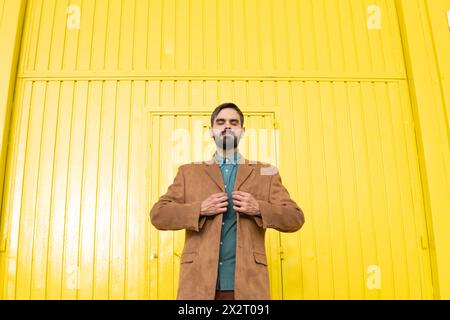 Man wearing brown jacket and standing in front of yellow wall Stock Photo