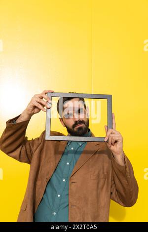 Smiling man wearing brown jacket and looking through photo frame Stock Photo