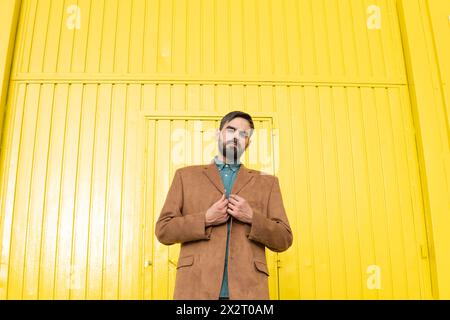Man wearing brown jacket and standing in front of yellow building Stock Photo