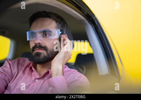 Man wearing smart glasses and sitting in car near yellow wall Stock Photo