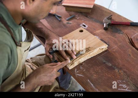 Carpenter carving on timber using chisel at workshop Stock Photo