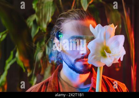Man wearing smart glasses with white flowers over face in front of plants Stock Photo