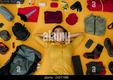 Happy woman lying near travel kit against yellow background Stock Photo