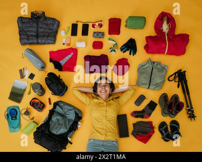Smiling woman lying near travel equipment against yellow background Stock Photo