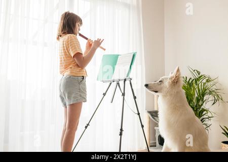 Girl playing flute near white Swiss Shepherd dog at home Stock Photo