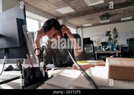 Happy businessman talking on landline phone at desk in office Stock Photo