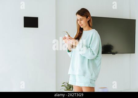 Woman standing and using smart phone at home Stock Photo