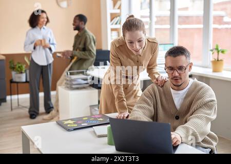 Smiling businesswoman helping colleague working on laptop in office Stock Photo