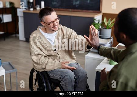 Happy businessman with disability giving high-five to colleague in office Stock Photo