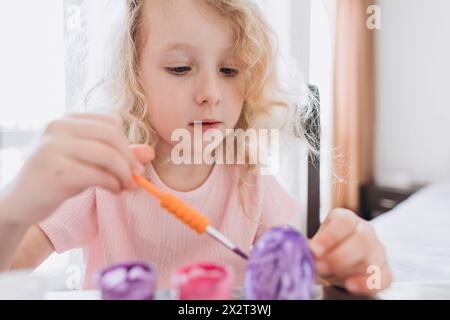 Blond girl coloring and decorating eggs for Easter at home Stock Photo