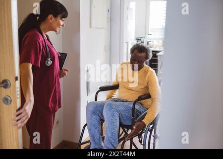Doctor in doorway looking at senior man in wheelchair Stock Photo
