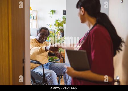 Smiling senior man in wheelchair handshaking with doctor at doorway Stock Photo