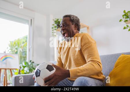 Happy senior man holding soccer ball watching match at home Stock Photo