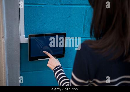 Woman using tablet PC mounted on blue wall outside house Stock Photo