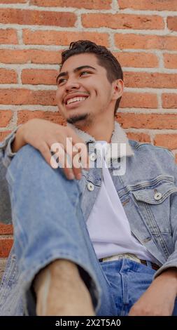 Smiling young man sitting near brick wall Stock Photo