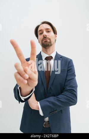 Confident mature businessman showing victory sign against white background Stock Photo