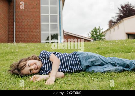 Happy boy lying down on grass in lawn Stock Photo
