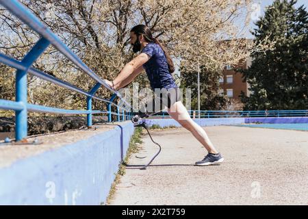 Athlete with prosthetic leg leaning on railing and stretching Stock Photo