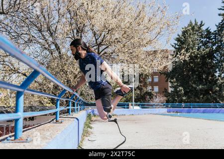 Athlete with artificial leg leaning on railing and stretching Stock Photo