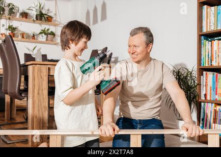 Smiling boy holding power tool by father assembling furniture at home Stock Photo