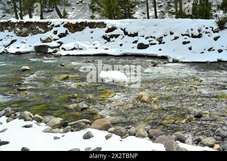 Frozen Baspa River bank with snow chunk on rock in the river, Chitkul, Himachal Pradesh, India. Winter landscape and clear freshwater scene. Stock Photo