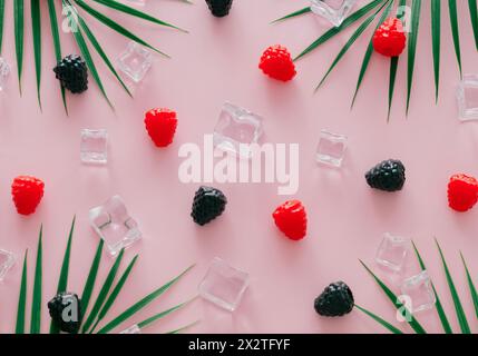 Creative summer pattern made of raspberries, blackberries, green tropical palm leaves and ice cubes on light pink background. Fruit minimal concept. Stock Photo