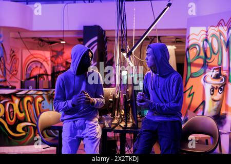 Hackers talking in abandoned warehouse, discussing malicious software development. African american and asian cyber criminals planning data breach and server password cracking cyberattack Stock Photo