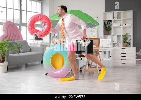 Happy male office worker with suitcase and inflatable rings running in office. Summer vacation concept Stock Photo