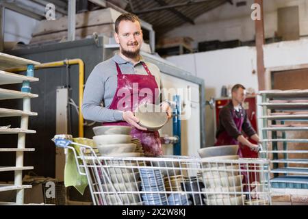 Successful potter displaying handcrafted plate in artisanal pottery studio Stock Photo