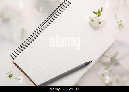 Guest list. Notebook, pencil and beautiful cherry tree blossoms on spring floral background, flat lay Stock Photo