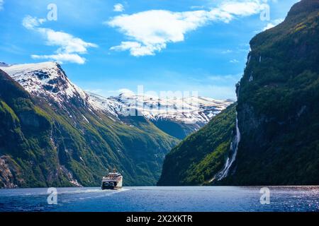 Boating the massive snow capped mountains and lush cliffs lined with green trees and waterfalls of the Geirangerfjord, Geiranger, Norway Scandinavia Stock Photo