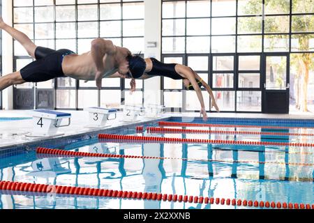 Diverse young swimmer competitors, including a Caucasian male and biracial female, diving into a poo Stock Photo