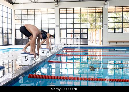 Diverse young swimmer competitors, including a Caucasian male and biracial female, preparing to dive Stock Photo