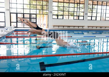 Diverse young swimmer competitors, indoors, wearing caps and goggles diving into a pool, copy space Stock Photo