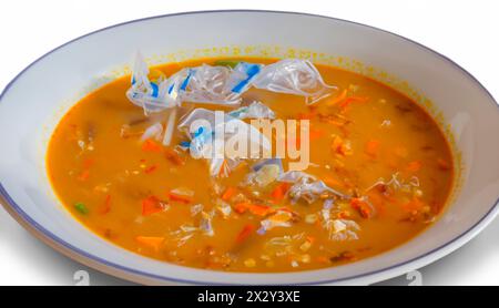 Soup plate filled with plastic soup, isolated on white. There is a large amount of plastic and other waste floating in it. Plastic soup problem Stock Photo