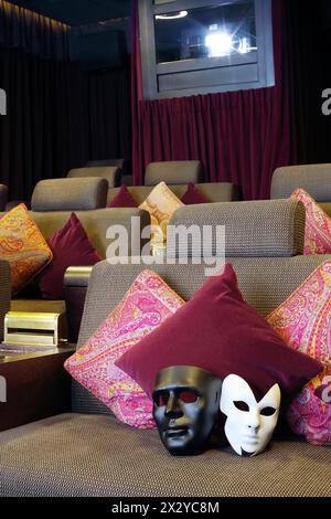 Black and white masks are on soft couch with pillows in movie theater. Stock Photo