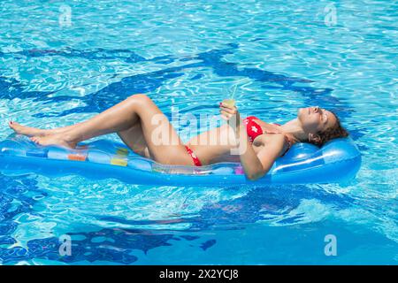 Woman swimming and relaxes in the pool on an inflatable mattress with a drink in hand Stock Photo