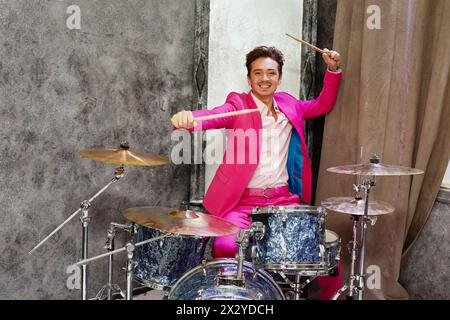 Young man in pink suit plays drums in room corner Stock Photo