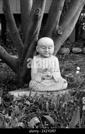 Granite sculpture of a Buddha and a rabbit sitting under a tree, black and white Stock Photo